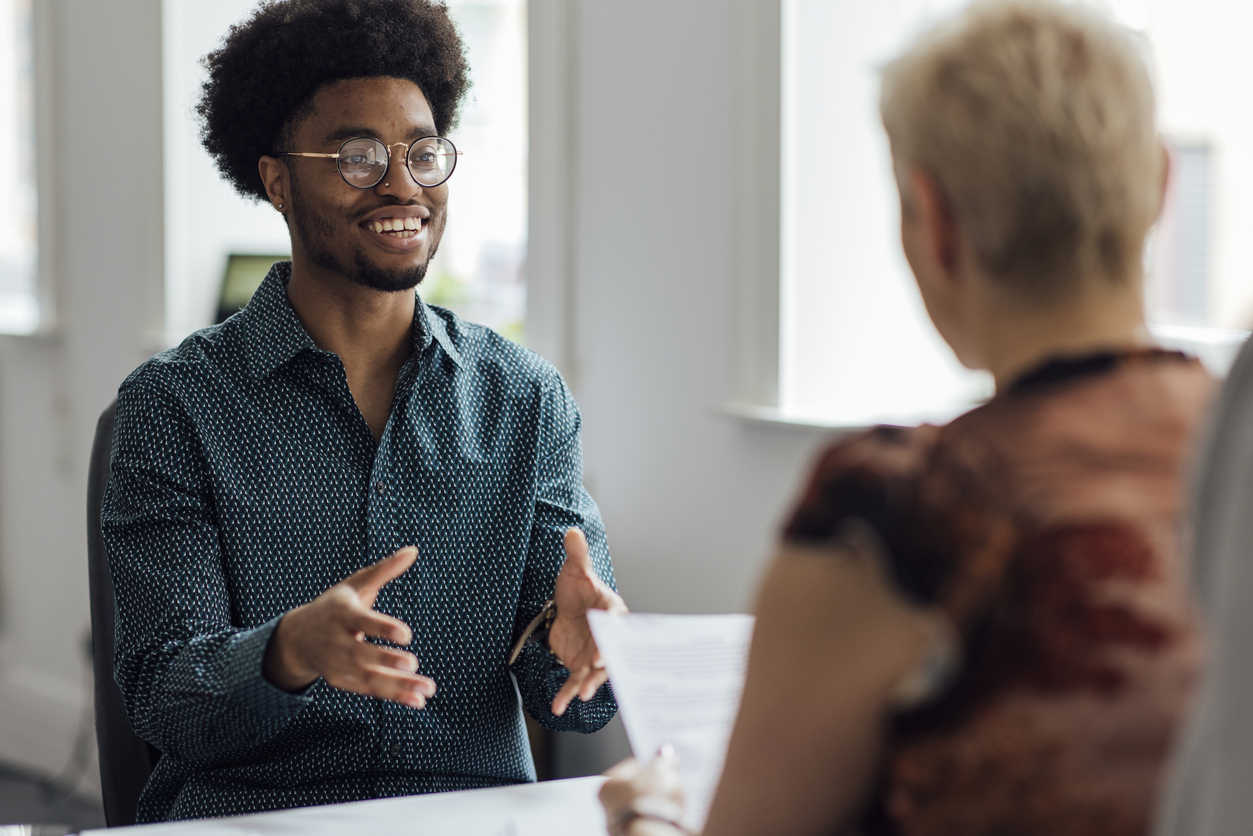 Over the shoulder view of a young male employee engaging in a focused discussion with a mature female manager at the managers desk in an office interior in Newcastle, England. They are wearing smart casual clothing. Videos also available for this scenario.